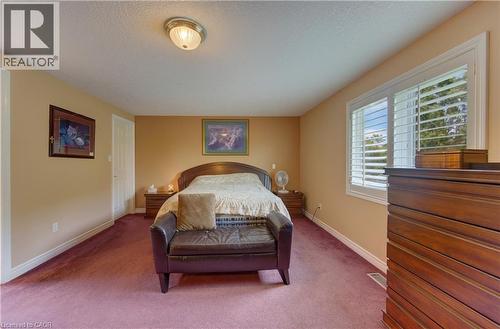 Spacious interior room featuring a large window with white louvered shutters, light beige wall paint, a flush-mount ceiling light fixture, and plum-colored carpeting - 599 Coldstream Drive, Waterloo, ON 