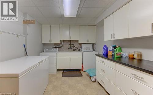 Functional laundry area featuring extensive white cabinetry, a utility sink, and ample countertop space with a dark finish - 599 Coldstream Drive, Waterloo, ON 