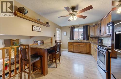 Kitchen featuring light wood-finish flooring, wood cabinetry with upper glass-front accents, and a granite-look countertop - 599 Coldstream Drive, Waterloo, ON 