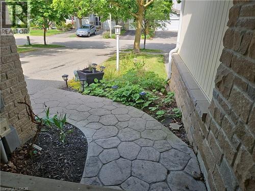Stamped concrete pathway with integrated landscape lighting, complemented by a stone facade and light-colored vertical siding - 596 Spinnaker Crescent, Waterloo, ON 
