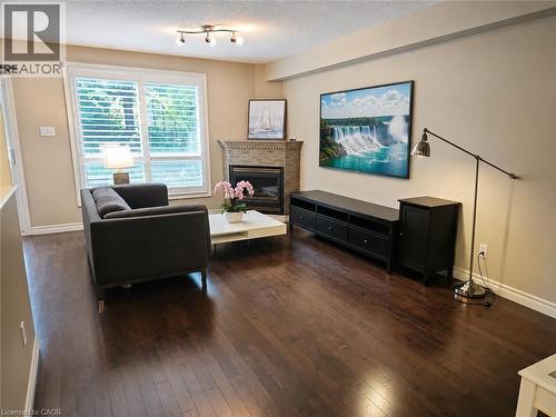 Open living space featuring dark wood-finish flooring, a fireplace with a stone surround and mantel, and a large window with white plantation shutters - 596 Spinnaker Crescent, Waterloo, ON 