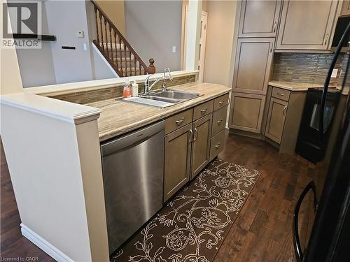 Kitchen featuring light brown cabinetry, stainless steel dishwasher, brown wood-finish flooring, and a stone countertop with a mosaic tile backsplash - 596 Spinnaker Crescent, Waterloo, ON 