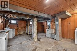 Basement area featuring wood paneling, exposed brick support column, concrete flooring, and visible utility systems - 