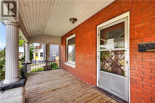 Covered porch with wood-finish flooring, brick exterior, fluted columns, and a decorative wrought iron railing - 26 Arthur Avenue, St. Thomas, ON - Outdoor With Deck Patio Veranda With Exterior