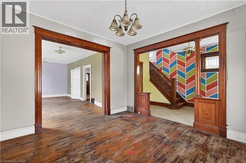 Hardwood flooring throughout the main level featuring an ornate chandelier, detailed wood trim, and a classic wood staircase - 26 Arthur Avenue, St. Thomas, ON - Indoor Photo Showing Other Room