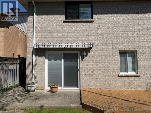 Rear exterior featuring brick facade, ground-level wood deck, concrete patio, and a sliding glass door with an overhead awning - 51 Redtail Crescent, Hamilton, ON 