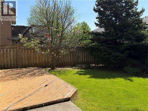 Expansive outdoor space featuring a large wooden deck, a lush green lawn, mature trees, and privacy fencing - 51 Redtail Crescent, Hamilton, ON 