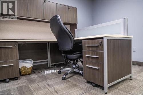 Modern office workstation featuring wood-finish cabinetry, integrated overhead storage, and a frosted glass partition - 5100 South Service Road, Burlington, ON 