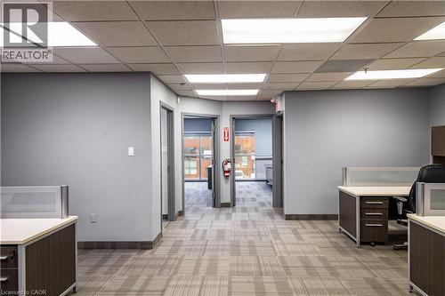 Open-concept workspace featuring patterned carpet flooring, neutral gray walls, and drop ceiling with integrated lighting - 5100 South Service Road, Burlington, ON 