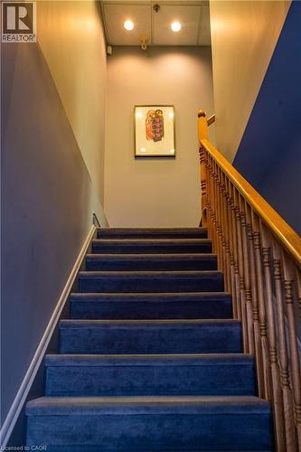Staircase featuring dark blue carpeted treads, wood banister, and painted walls - 5100 South Service Road, Burlington, ON 