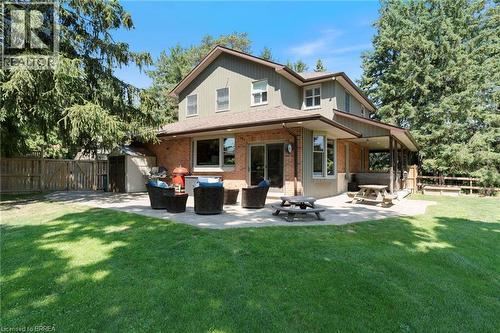 Expansive backyard featuring a large paved patio, covered porch area, lush green lawn, and mature trees providing natural screening - 182 Governors Road E, Paris, ON 