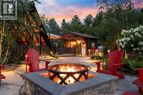 Stone paver patio featuring a built-in fire pit with stone surround, perimeter landscape lighting, an A-frame structure, and a separate detached accessory building - 182 Governors Road E, Paris, ON 