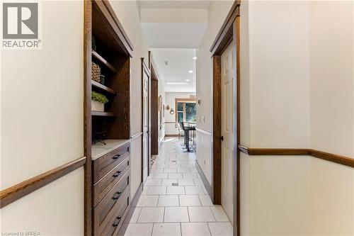 Hallway featuring light-toned tile flooring with dark accent tiles, built-in wooden cabinetry with open shelving and drawers, white panel doors, and rich wood trim - 182 Governors Road E, Paris, ON 
