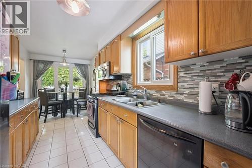 Galley kitchen with wood cabinetry, tile flooring, mosaic tile backsplash, double basin sink, and stainless steel appliances - 817 Acadia Drive, Hamilton, ON - Indoor Photo Showing Kitchen With Double Sink