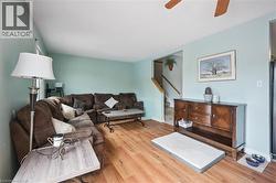 Spacious living area featuring wood-finish flooring, light blue wall paint, and a ceiling fan - 