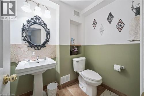 Pedestal sink with chrome fixtures, an ornate dark-framed mirror, and a three-light vanity fixture - 817 Acadia Drive, Hamilton, ON - Indoor Photo Showing Bathroom