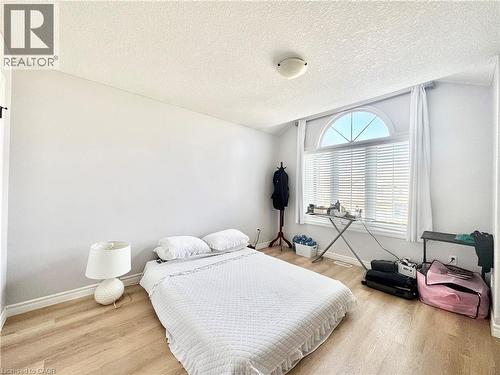 Room featuring an arched window with integrated blinds and white drapes, wood-finish flooring, and light-toned walls - 1333 Countrystone Drive, Kitchener, ON 