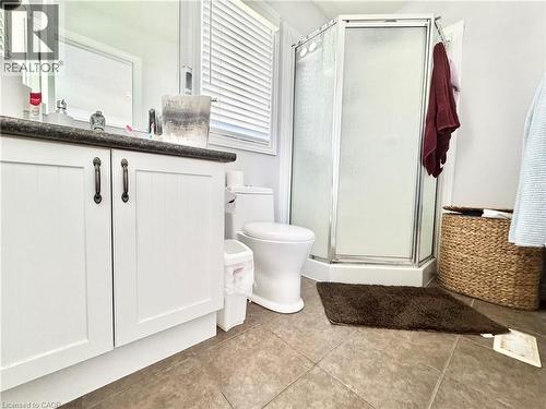 Bathroom featuring a white vanity with dark countertop, a corner shower enclosure with frosted glass, and tiled flooring - 1333 Countrystone Drive, Kitchener, ON 