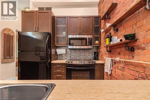 Kitchen featuring a brick accent wall, wood-finish cabinetry, stainless steel microwave, and textured backsplash - 18 Pearl Street S, Hamilton, ON 