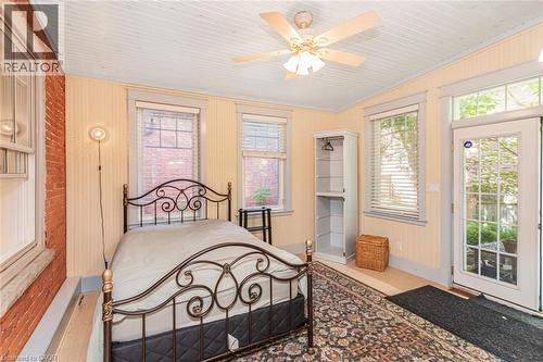 Room featuring exposed brick wall, three windows with blinds, light wood-finish flooring, and a glass-paned door - 18 Pearl Street S, Hamilton, ON 