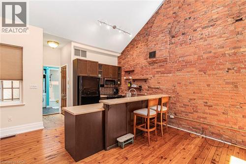 Exposed brick wall kitchen featuring wood-finish flooring, dark cabinetry, and a breakfast bar with built-in storage - 18 Pearl Street S, Hamilton, ON 