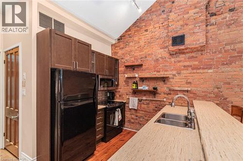 Kitchen featuring an exposed brick wall, wood-finish flooring, dark wood cabinetry, a double basin stainless steel sink, and light wood-finish countertops - 18 Pearl Street S, Hamilton, ON 