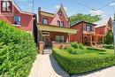 Brick exterior featuring a gabled roofline, covered front porch, and a manicured hedge-lined front garden - 16 Mulberry Street, Hamilton, ON 