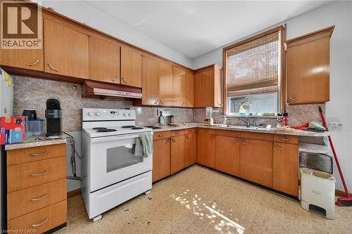 Kitchen featuring extensive wood cabinetry, a white electric range, a double basin stainless steel sink, and patterned countertops - 16 Mulberry Street, Hamilton, ON 