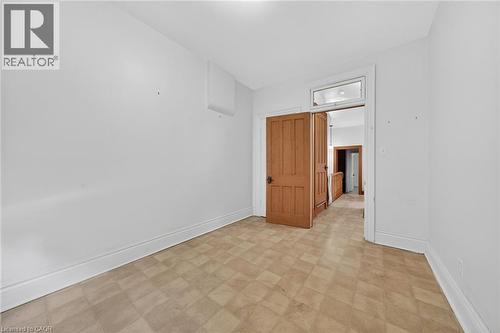 Room featuring light-toned resilient flooring, white baseboards, and a solid wood paneled door with dark hardware - 16 Mulberry Street, Hamilton, ON 