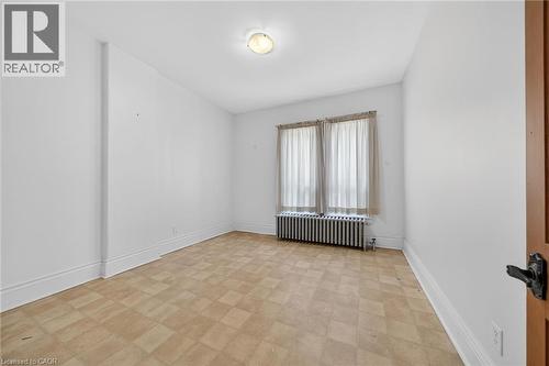 White-walled room featuring a checkered floor, built-in radiator, and central ceiling light fixture - 16 Mulberry Street, Hamilton, ON 