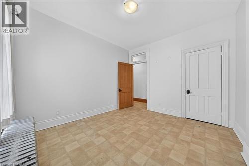 Room featuring patterned tile flooring, a white paneled door with matte black hardware, a natural wood-finish door, and a traditional baseboard radiator beneath a window - 16 Mulberry Street, Hamilton, ON 