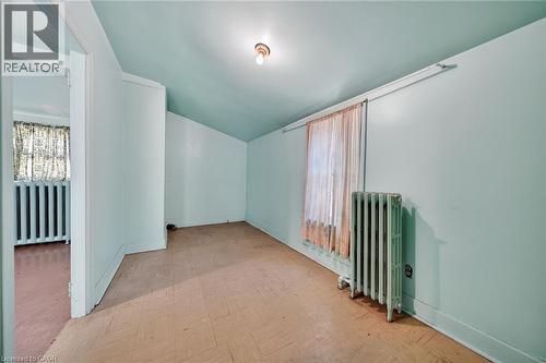 Room featuring an angled ceiling, window with a radiator below, and parquet-style flooring - 16 Mulberry Street, Hamilton, ON 