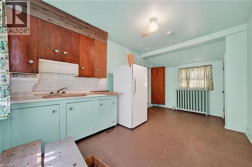 Kitchen area featuring wood-finish upper cabinetry, light green lower cabinetry, and a sink with a backsplash - 16 Mulberry Street, Hamilton, ON 