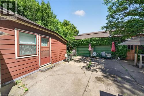 Paved patio area featuring mature perimeter trees, a red wood-sided structure with a screen door, and a green vine-covered structure with a wood gate - 16 Mulberry Street, Hamilton, ON 