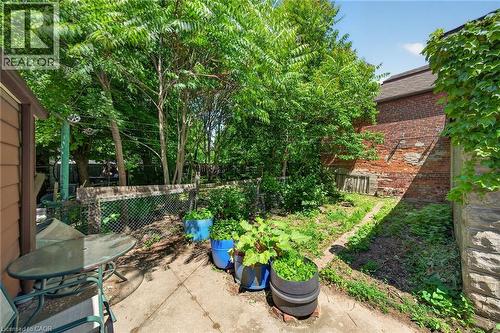 Outdoor patio area with concrete surfacing, surrounded by mature greenery and a brick-faced exterior wall with stone foundation - 16 Mulberry Street, Hamilton, ON 