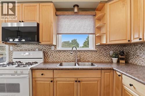 Kitchen featuring light wood cabinetry, stone-finish countertops, stainless steel sink with a gooseneck faucet, mosaic tile backsplash, and an over-the-range microwave - 116 Scott Road, Cambridge, ON 