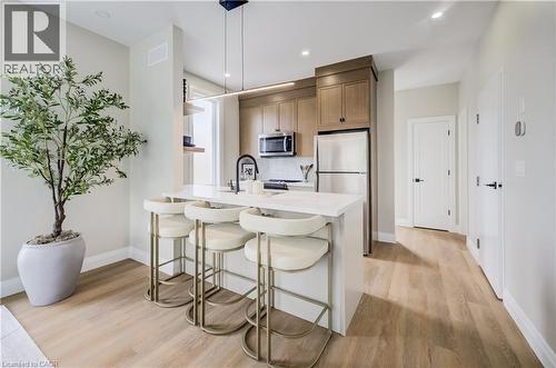 Modern kitchen featuring light wood-finish flooring, a white countertop island with seating, stainless steel appliances, and wood cabinetry - 210 Heritage Drive Unit# Upper, Kitchener, ON 