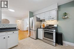 Kitchen featuring stainless steel appliances, white cabinetry with dark hardware, dark countertops, and a mosaic tile backsplash - 