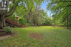 Expansive backyard featuring a large grassy area, mature trees, and a multi-level wood deck with stairs - 