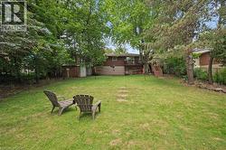 Spacious backyard featuring a lush green lawn, mature trees providing natural screening, and a raised deck with exterior stairs - 