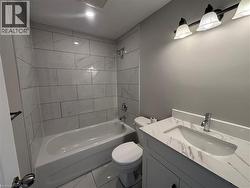 Bathroom featuring a white bathtub with subway tile surround, tile flooring, a single vanity with a white countertop and integrated sink, and a three-light fixture - 