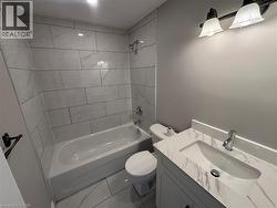 Bathroom featuring subway-style tiled shower surround, a white built-in bathtub, and a vanity with an integrated sink and marbled countertop - 