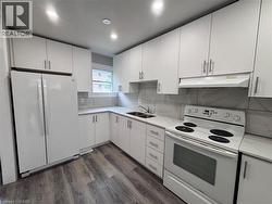 Modern kitchen featuring white cabinetry with brushed nickel hardware, light-toned countertops, a white electric range, and wood-finish flooring - 