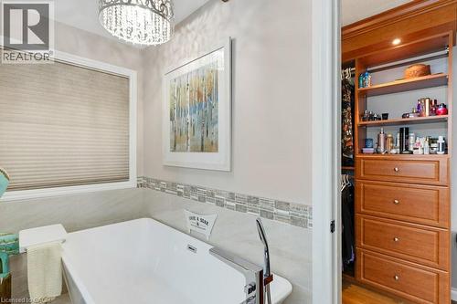 Freestanding soaking tub with polished chrome floor-mounted faucet, mosaic tile accent band, and an adjacent built-in closet system featuring warm wood cabinetry and integrated lighting - 3786 Old Beverly Road, North Dumfries, ON 