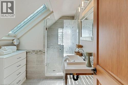 Bathroom featuring a skylight, glass-enclosed shower with decorative tile, single vanity with vessel sink, and wood-finish door - 3786 Old Beverly Road, North Dumfries, ON 