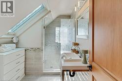 Bathroom featuring a skylight, glass-enclosed shower with decorative tile, single vanity with vessel sink, and wood-finish door - 