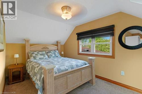 Sloped ceiling bedroom featuring a double-pane window with wood trim, neutral wall color, and carpet flooring - 3786 Old Beverly Road, North Dumfries, ON 