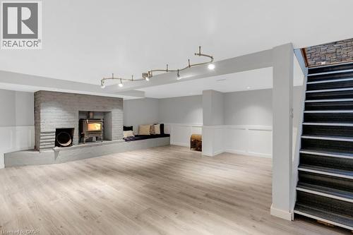 Expansive finished lower level featuring light wood-finish flooring, a painted brick fireplace with a wood-burning stove, and a built-in bench seating area - 3786 Old Beverly Road, North Dumfries, ON 