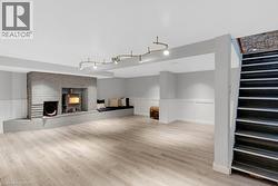 Expansive finished lower level featuring light wood-finish flooring, a painted brick fireplace with a wood-burning stove, and a built-in bench seating area - 