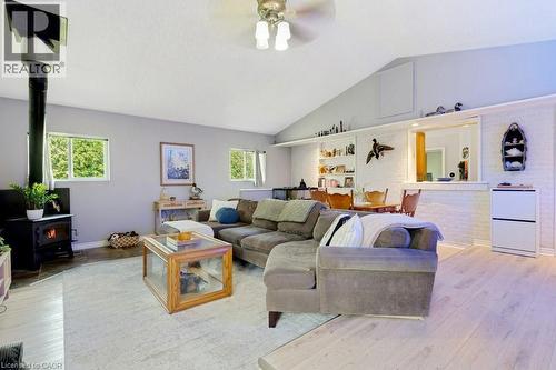 Apartment Spacious living area featuring a vaulted ceiling with a ceiling fan, a freestanding wood-burning stove, light wood-finish flooring, and white brick detailing - 3786 Old Beverly Road, North Dumfries, ON 